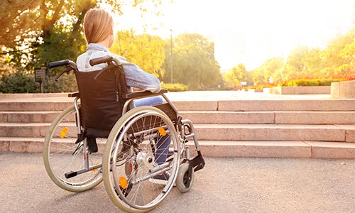 Mujer en silla de ruedas frente a una serie de escalones que le bloquean el paso.